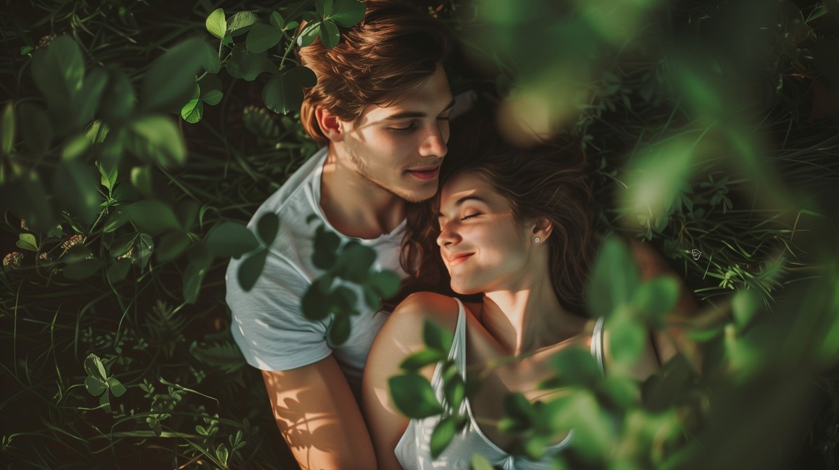 Frua und Mann auf Gras zwischen Bäumen, die gemeinsam kuscheln und sich umarmen.