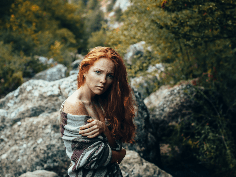 Frau mit roten Haaren in den Bergen in der Natur, die ernst zur Seite schaut.