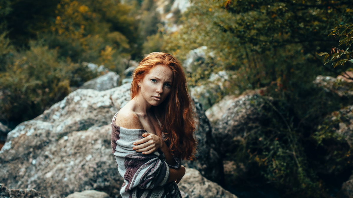 Frau mit roten Haaren in den Bergen in der Natur, die ernst zur Seite schaut.