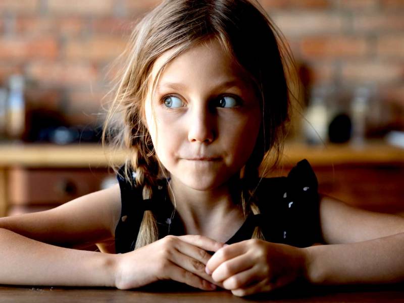 Mädchen, ca 7 Jahre, sitzt mit einem schuldbewussten Blick am Tisch.