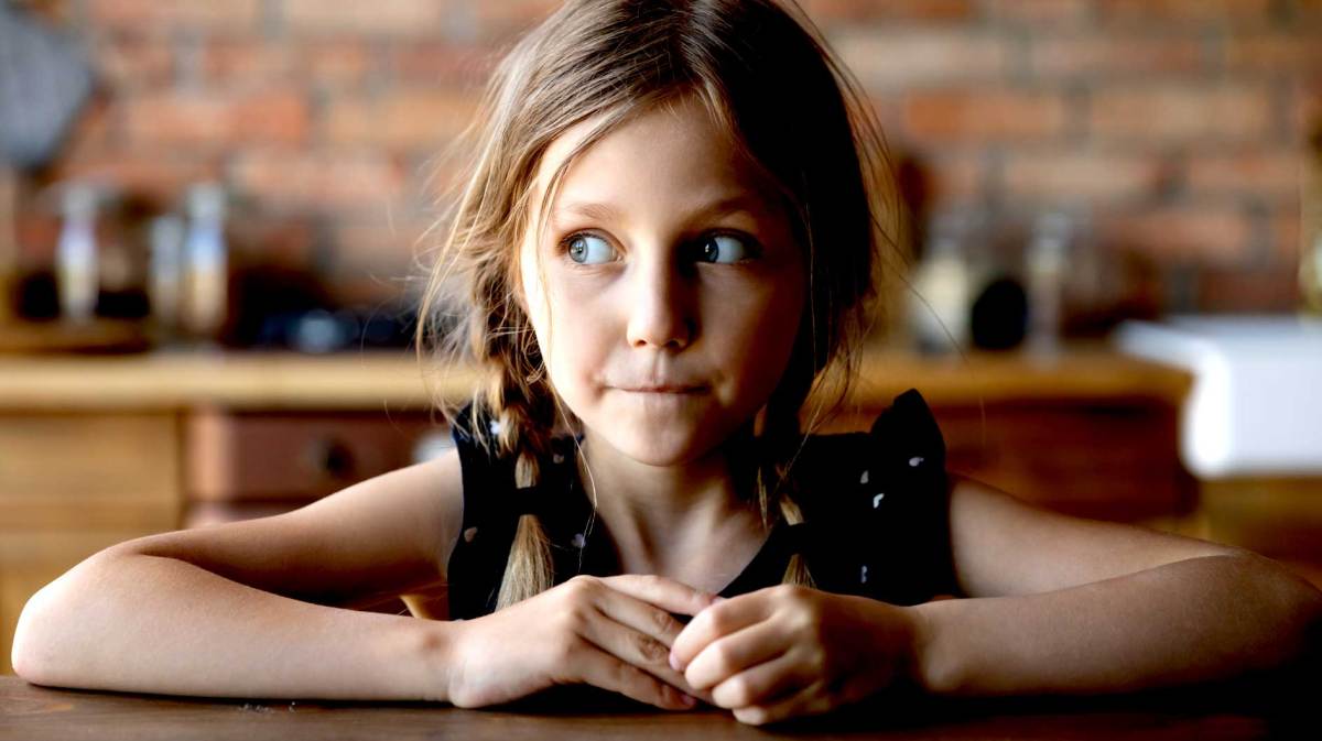 Mädchen, ca 7 Jahre, sitzt mit einem schuldbewussten Blick am Tisch.