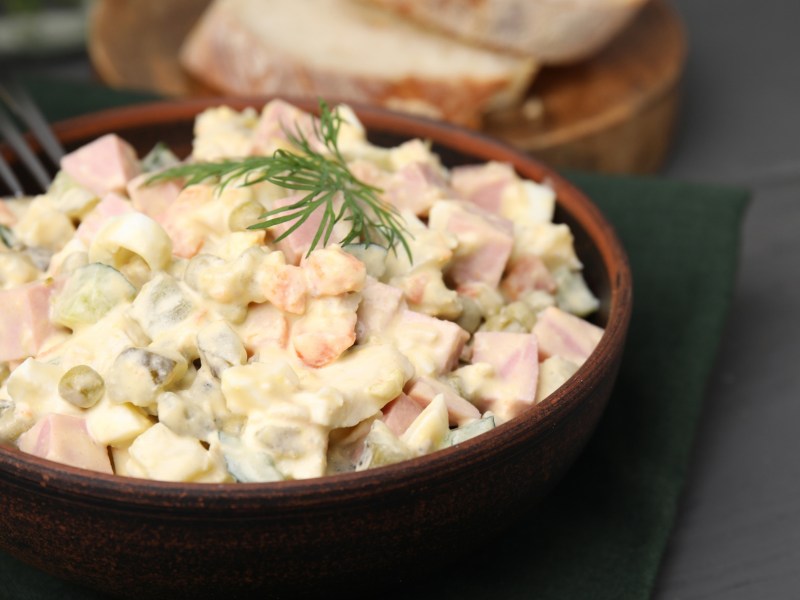 Kartoffelsalat mit Fleischwurst, Erbsen und Dill in einer Holzschüssel.