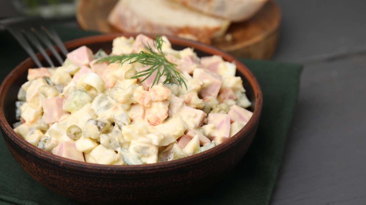 Kartoffelsalat mit Fleischwurst, Erbsen und Dill in einer Holzschüssel.