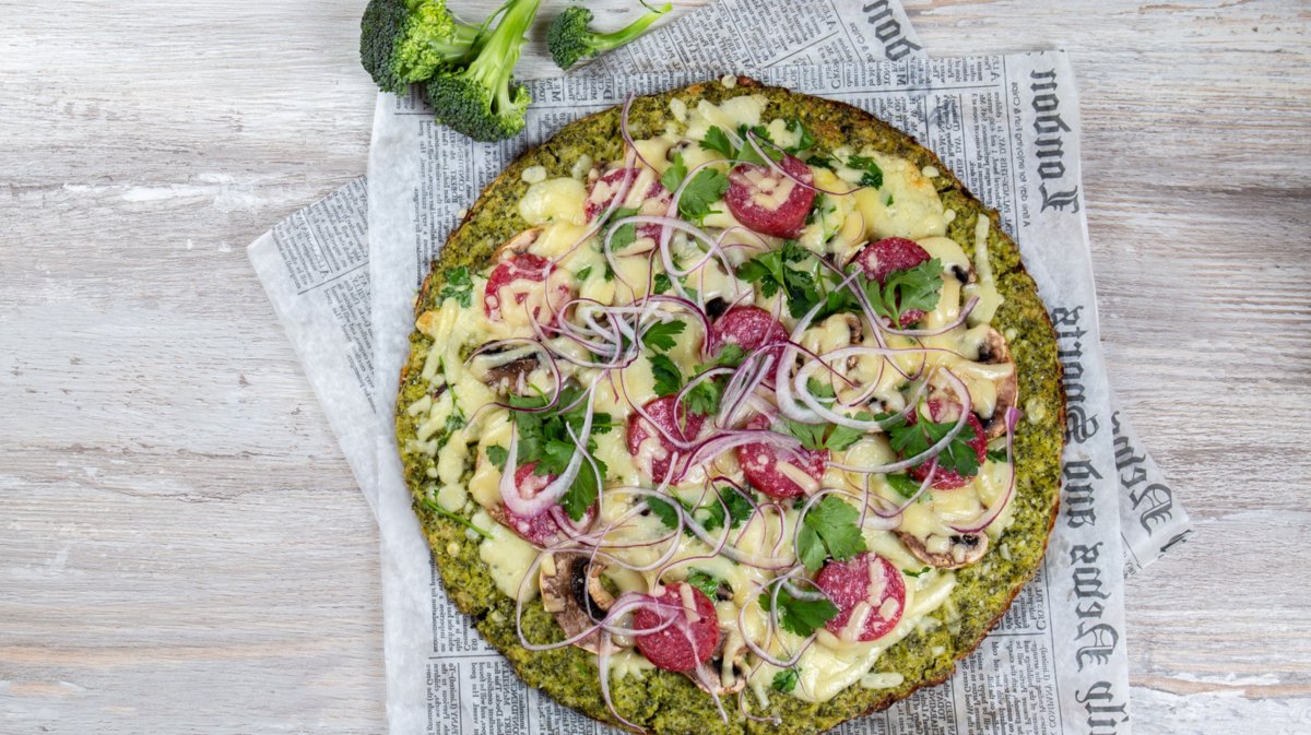 Pizza mit Brokkoli-Boden auf einem Stück Zeitungspapier auf einem Tisch.