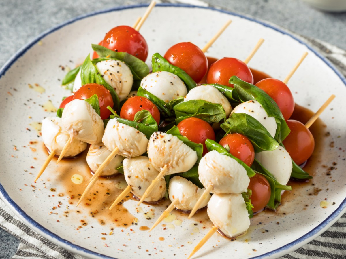 Spieße mit Tomate, Mozzarella, Basilikum auf einem weißen Teller.