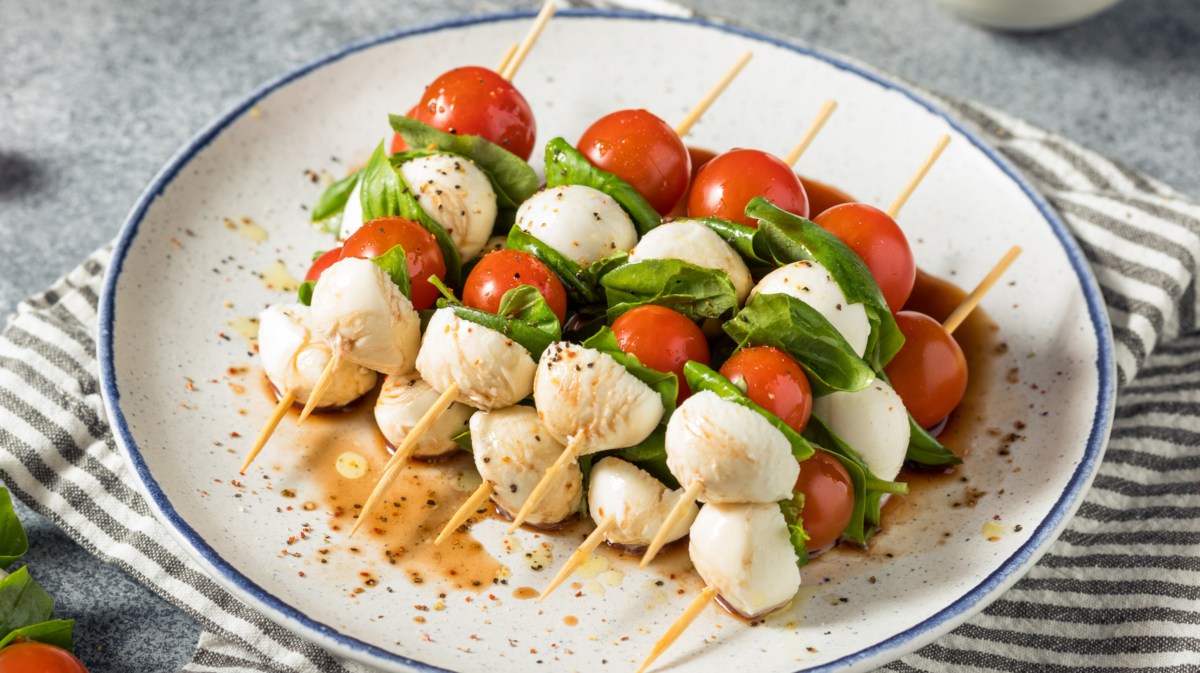 Spieße mit Tomate, Mozzarella, Basilikum auf einem weißen Teller.