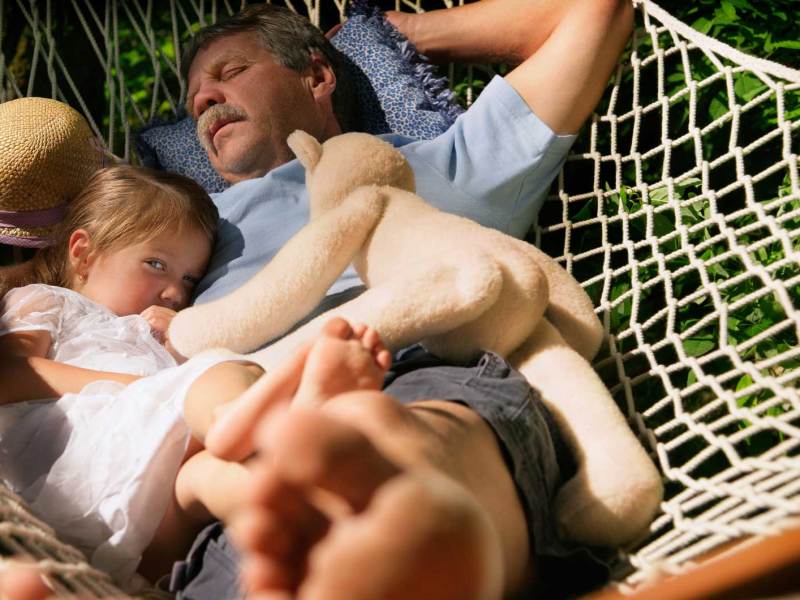 Vater und Tochter liegen in der Hängematte. Er ist eingeschlafen, sie schielt vorsichtig Richtung Kamera.