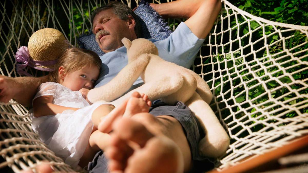 Vater und Tochter liegen in der Hängematte. Er ist eingeschlafen, sie schielt vorsichtig Richtung Kamera.