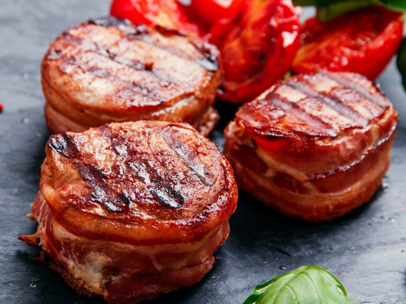 Schweinefilets mit Speck umwickelt vom Grill auf einer schwarzen Schieferplatte.