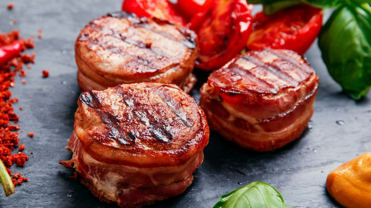 Schweinefilets mit Speck umwickelt vom Grill auf einer schwarzen Schieferplatte.