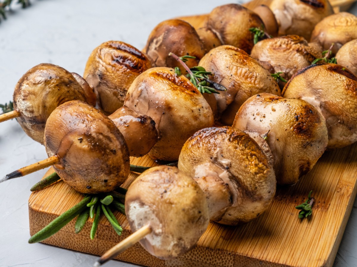 Gegrillte Champignons Spieße auf einem Holzbrett.