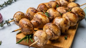 Gegrillte Champignons Spieße auf einem Holzbrett.