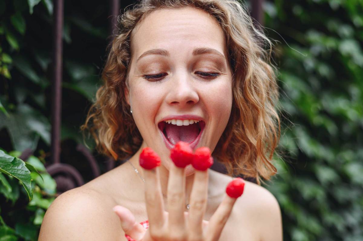 Nahaufnahme einer glücklichen jungen Frau mit Himbeeren an den Fingern.