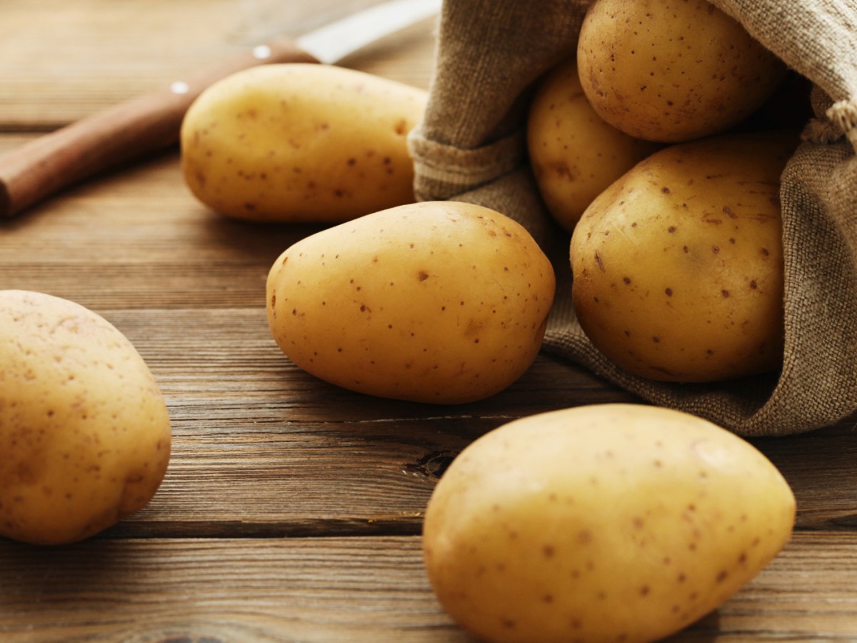 Rohe Kartoffeln liegen auf Holztisch, rollen aus Jutesack.