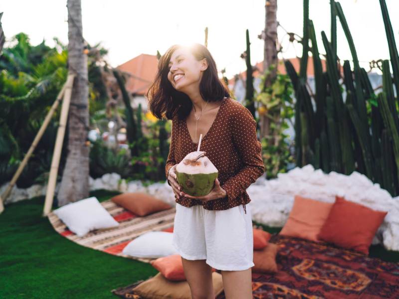 Fröhliche junge Frau mit frischer Kokosnuss zum Trinken, die den Sommerabend genießt