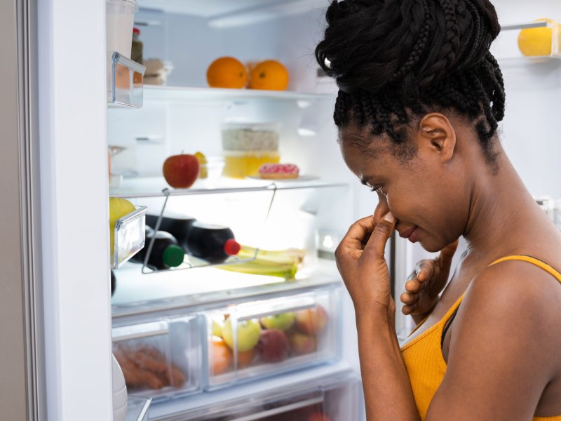 Frau steht vor Kühlschrank und hält sich die Nase zu als Symbolbild für "Kühlschrank stinkt"