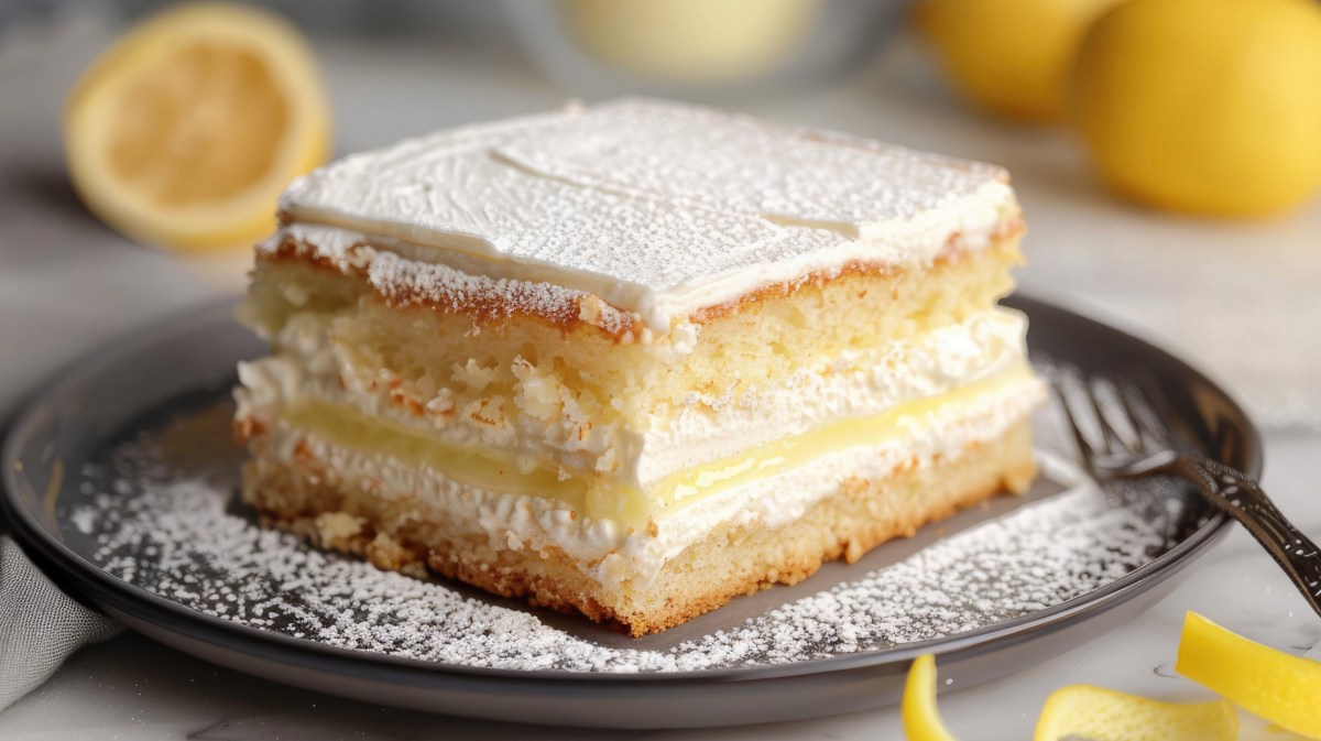 Kuchen mit Sahne in der Mitte und einer Zitronencreme, mit Puderzucker bestäubt auf einem dunklen Teller.