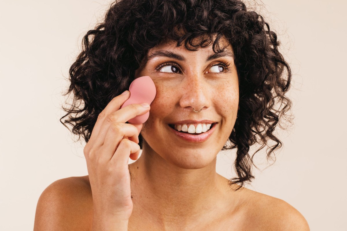 Frau mit lockigem braunen Haar benutzt rosa Beauty Blender