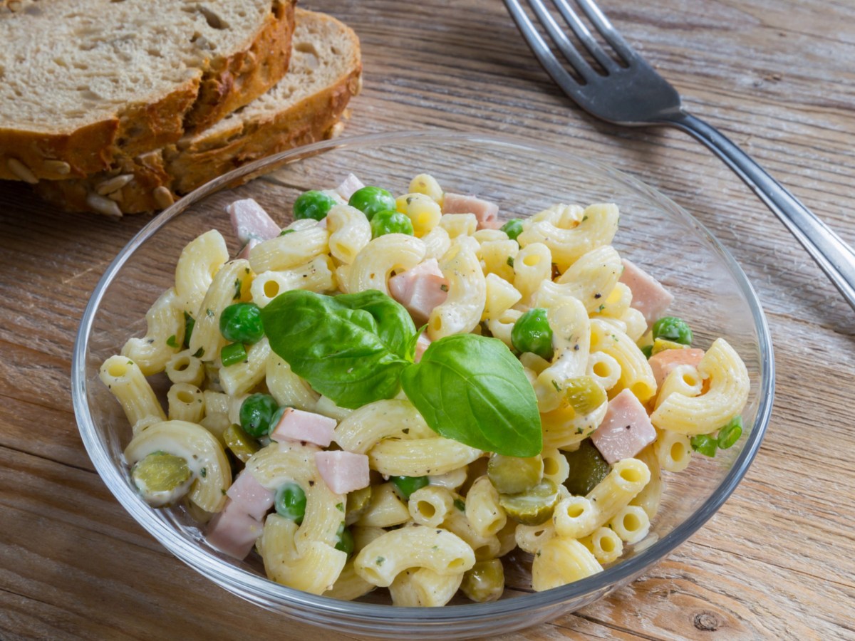 Nudelsalat in Glasschüssel mit Fleischwurst, Erbsen und Gurken.