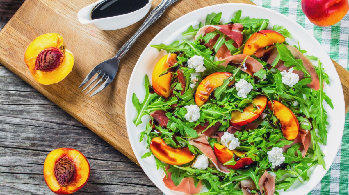 Ruculasalat mit Pfirsichen und Burrata auf einem großen weißen Teller.