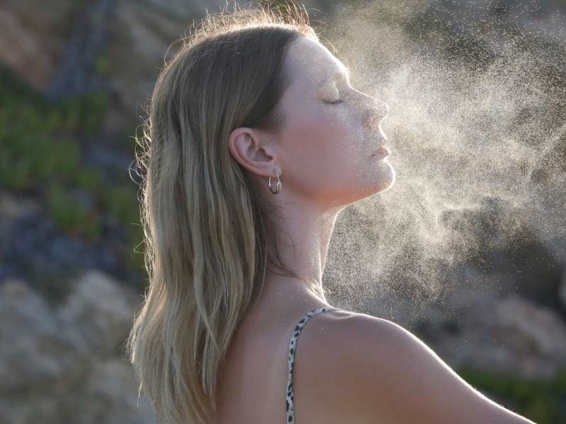 Frau sprüht Gesichtsnebel auf ihr Gesicht, sommerliches Hautpflegekonzept