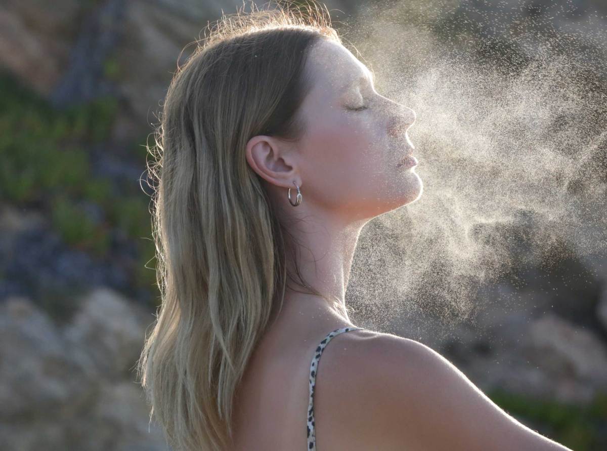 Frau sprüht Gesichtsnebel auf ihr Gesicht, sommerliches Hautpflegekonzept