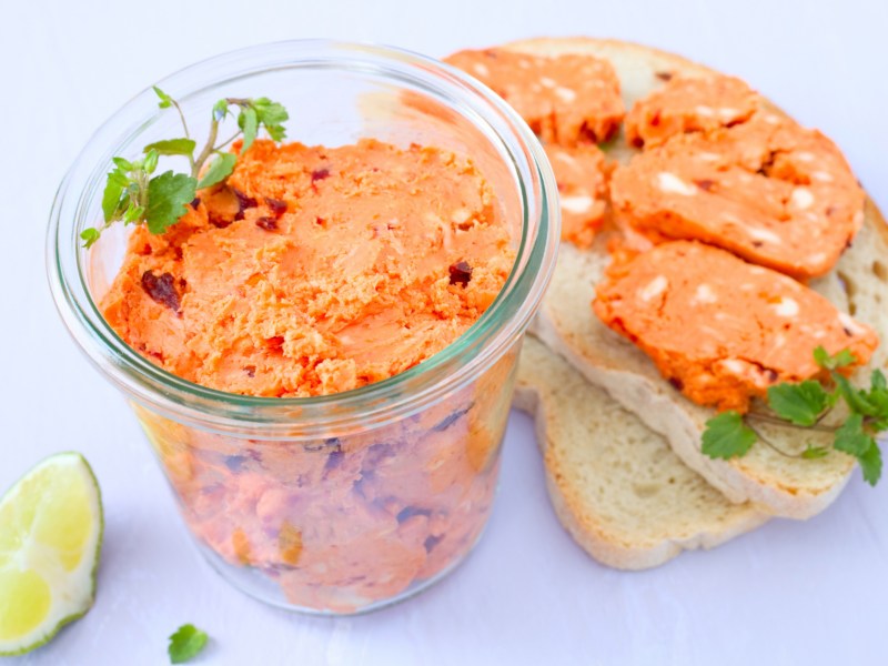 Tomatenbutter in einem Glasgefäß, daneben zwei Scheiben Brot mit Tomatenbutter.