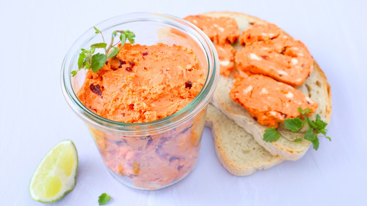 Tomatenbutter in einem Glasgefäß, daneben zwei Scheiben Brot mit Tomatenbutter.