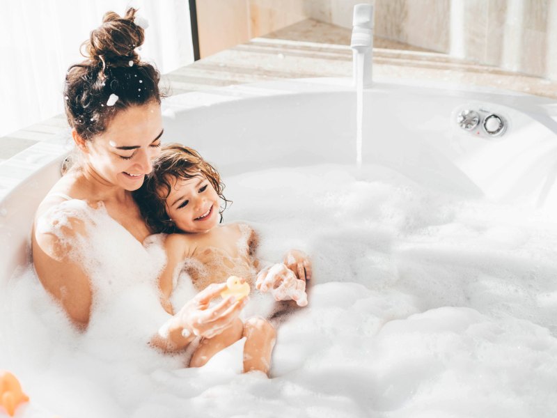 Mutter und Kind baden gemeinsam in einer Badewanne voller Schaum.