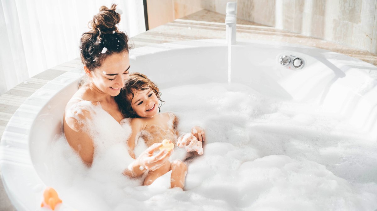 Mutter und Kind baden gemeinsam in einer Badewanne voller Schaum.