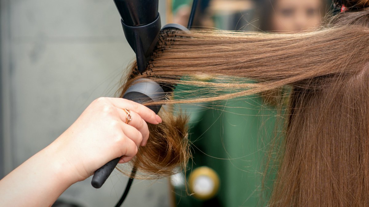 Friseurin föhnt Frau die Haare über eine Rundbürste