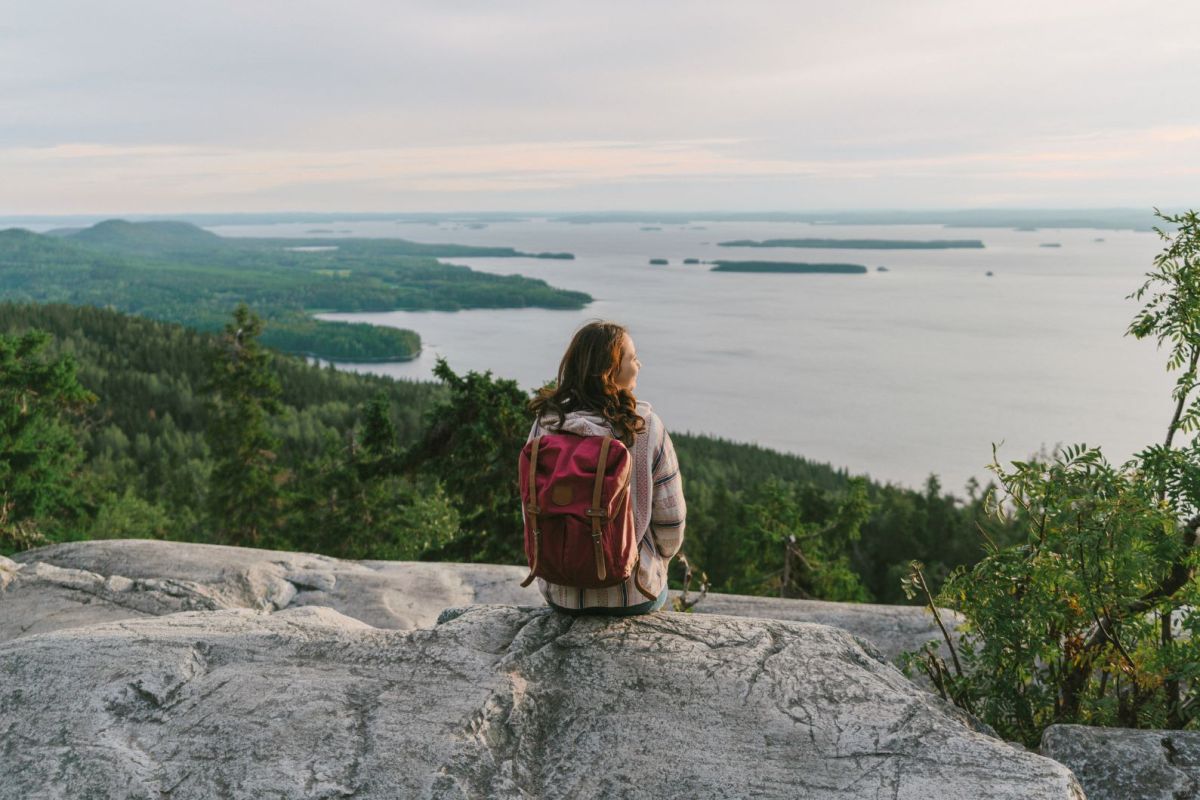 Eine Frau mit Rucksatz sitzt auf einer Klippe und schaut zum Horizont