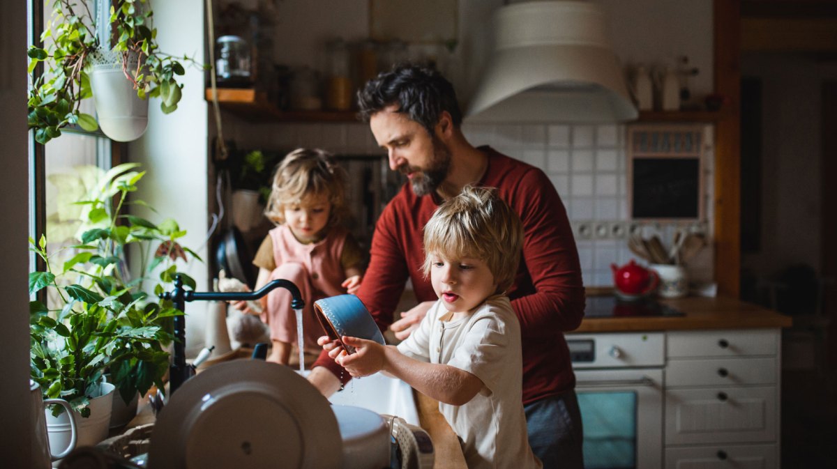 Vater macht zu Hause den Abwasch mit seinen beiden kleinen Kindern.