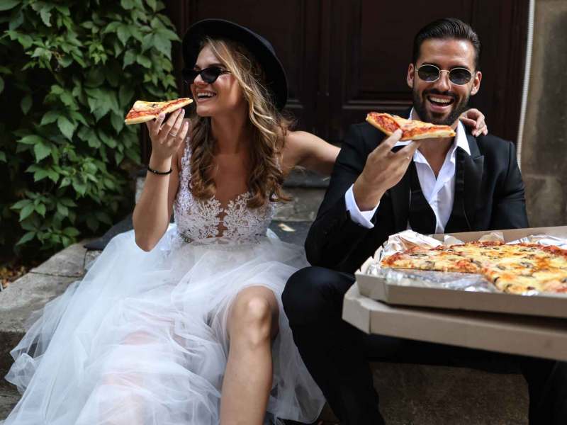 Brautpaar sitzt auf einer Stufe und isst gemeinsam Pizza.