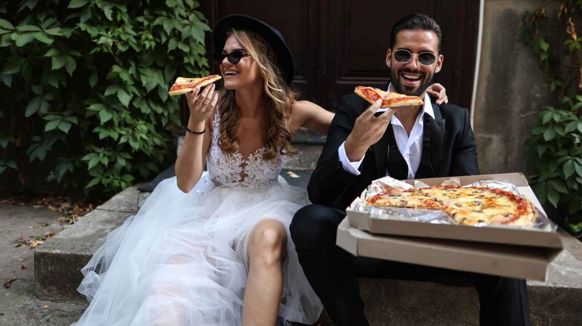 Brautpaar sitzt auf einer Stufe und isst gemeinsam Pizza.