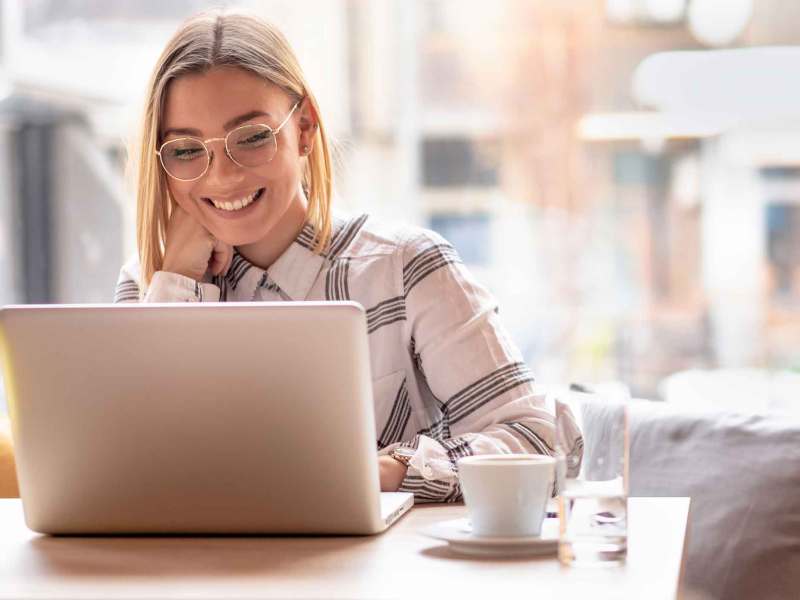 Blonde Frau mit Brille sitzt in einem Cafe vor dem Laptop und hat ein Meeting.