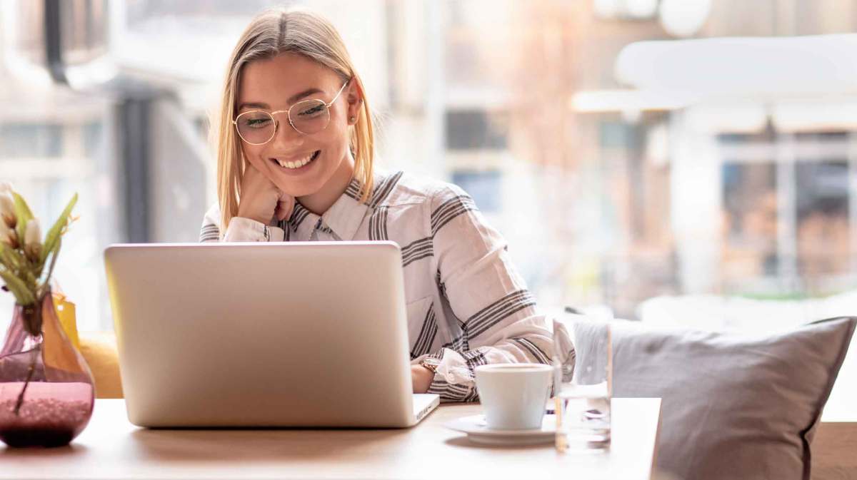 Blonde Frau mit Brille sitzt in einem Cafe vor dem Laptop und hat ein Meeting.