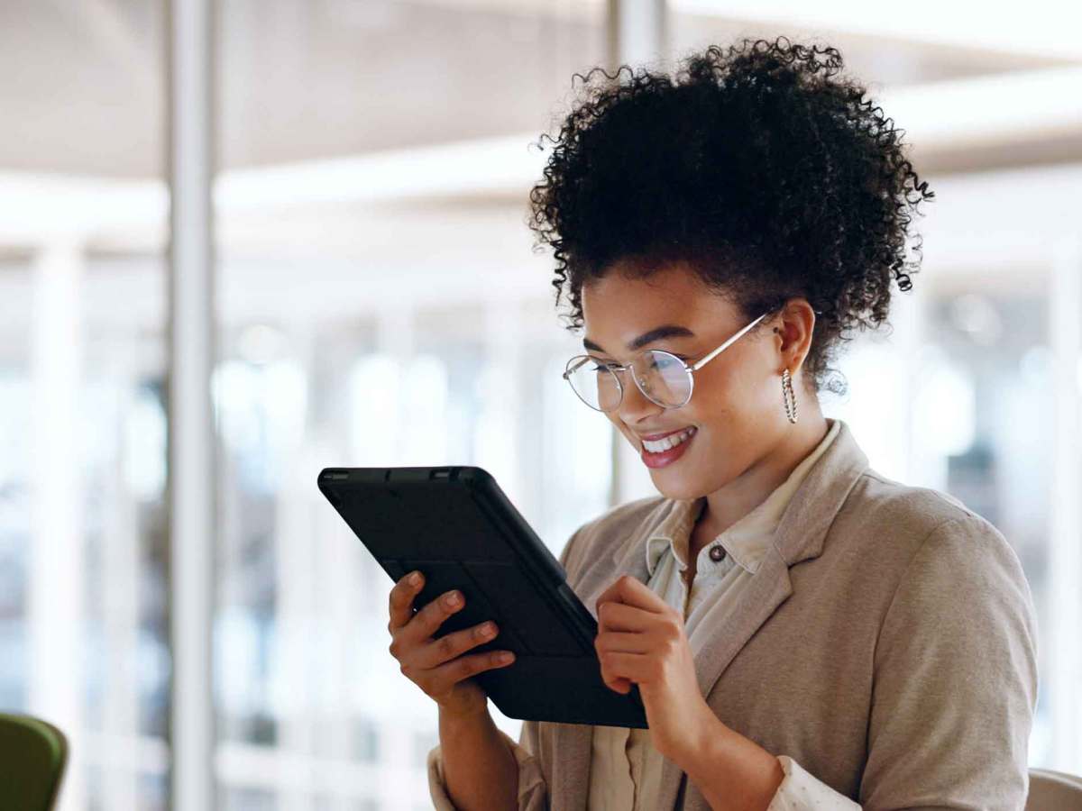 Junge Frau mit Brille steht auf der Arbeit und hält ein Tablet in der Hand.