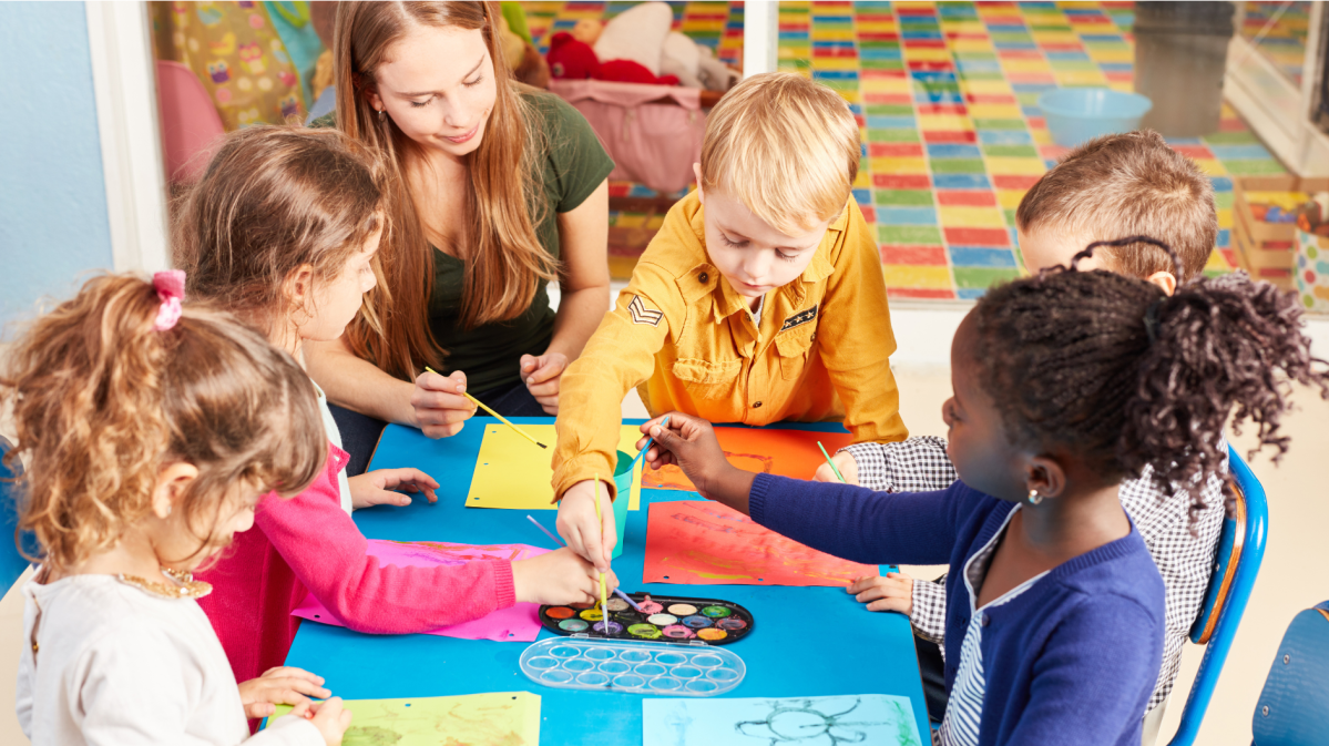 Kleinkinder sitzen an einem kleinen Tisch und malen mit ihrer Erzieherin