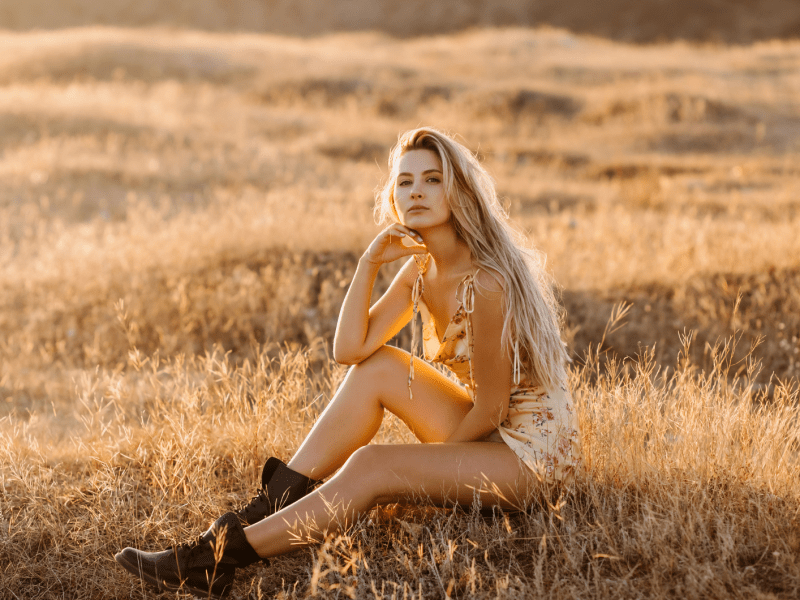 Frau auf einem Feld im Sonnenuntergang, die mit ernstem Blick zur Seite schaut.