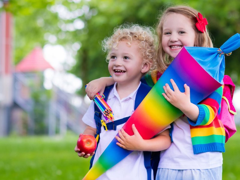 Zwei Geschwister mit einer Schultüte mit Regenbogenmuster an ihrem ersten Schultag.