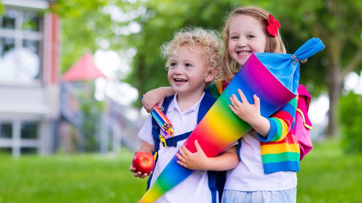 Zwei Geschwister mit einer Schultüte mit Regenbogenmuster an ihrem ersten Schultag.