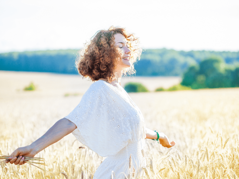 Frau auf einem Feld mit roten, gelockten Haaren, die zur Seite lacht.