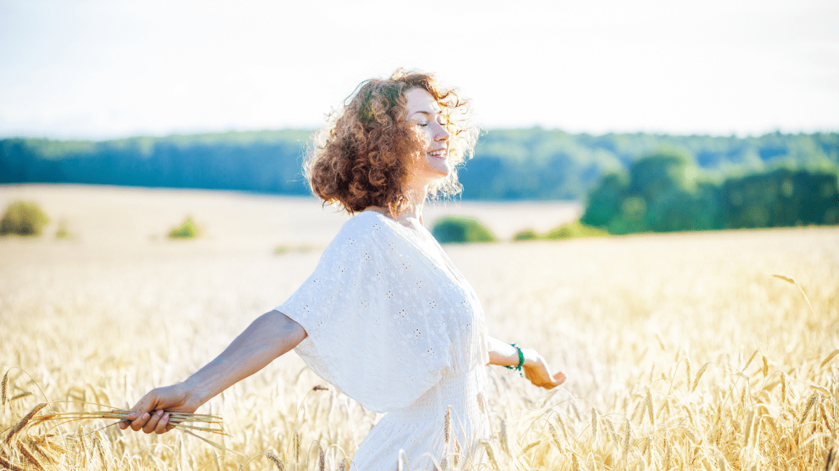 Frau auf einem Feld mit roten, gelockten Haaren, die zur Seite lacht.