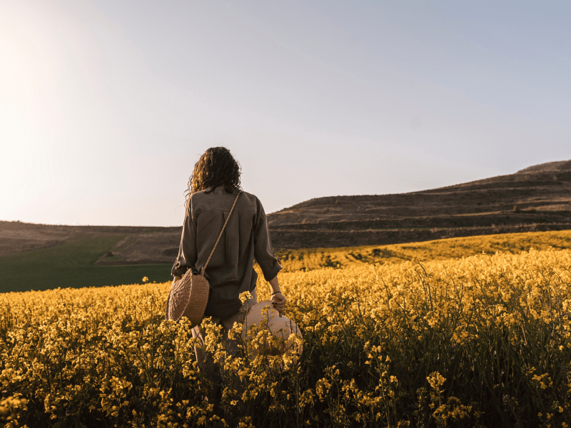 Frau in einem Feld voller gelber Blumen, die mit dem Rücken zur Kamera steht.