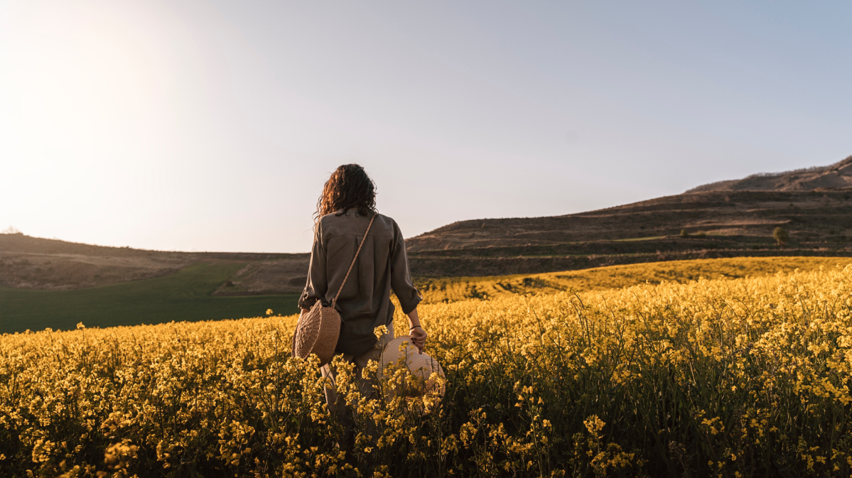 Frau in einem Feld voller gelber Blumen, die mit dem Rücken zur Kamera steht.