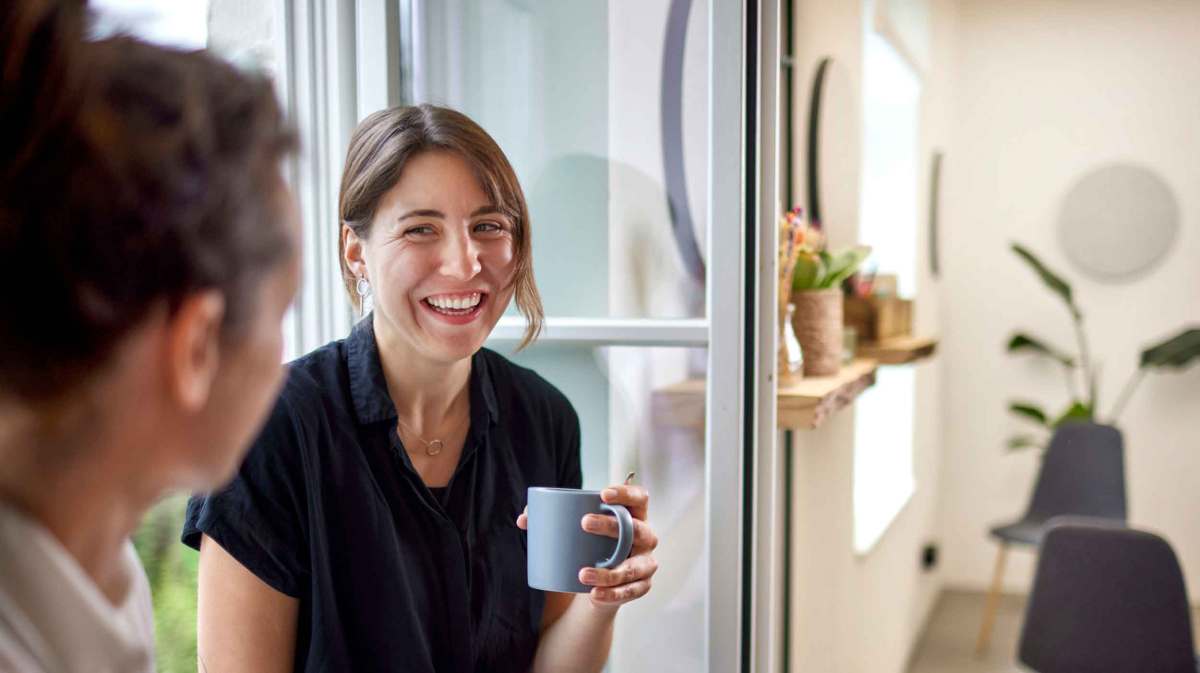 Frau sitzt auf einer Fensterbank mit einer Kollegin und lacht.