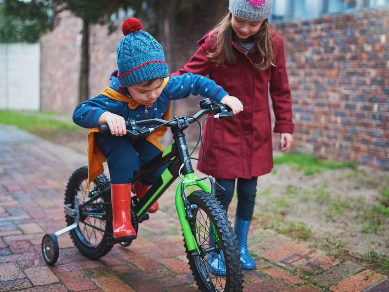 Große Schwester hilft kleinem Bruder beim Fahrradfahren.