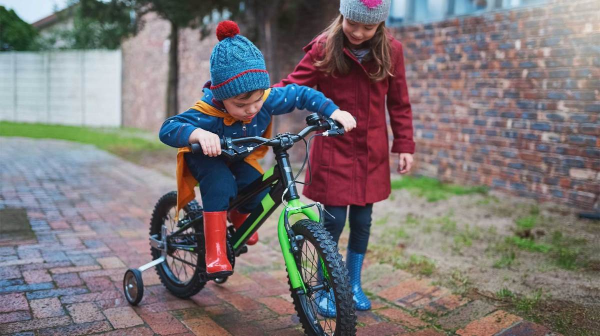 Große Schwester hilft kleinem Bruder beim Fahrradfahren.