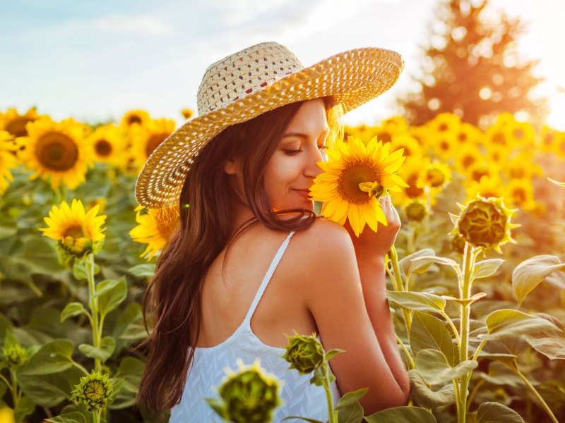 Frau mit Strohhut im Sonnenblumenfeld